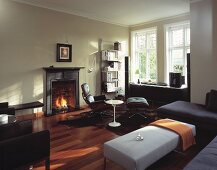 English living room with fire in fireplace, sofas, ottomans, easy chairs and retro table
