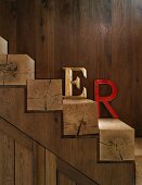 Farbige Deko Buchstaben auf Stufen aus Vierkantholz an Holzwand lehnend