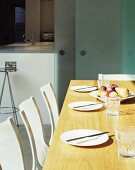 Gedeckter Tisch und weiße Stühle vor offener Schiebtür aus opakem Glas