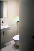 View through open door to small designer bathroom with sink and toilet