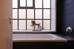 View through open door to bathtub with horse figurine in shiny metal on windowsill