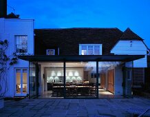 Modern, illuminated glass extension in the evening looking into an open-plan dining room