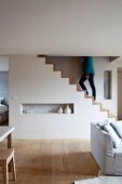 White, maisonette apartment in modern, Scandinavian style with waxed wooden floor and woman walking up sculptural staircase installation in background