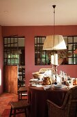 Pendant lamp with white lampshade above set table in dining room with dusky pink wall and integrated interior windows
