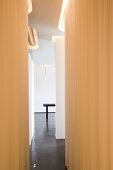 Narrow corridor with white walls and curtains bathed in warm light from recessed slots on ceiling