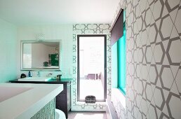 Contemporary designer bathroom in white and brown with graphic wallpaper and turquoise window tingeing the sunlight