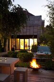 Terrace with outdoor furniture in front of lit fire bowl at twilight