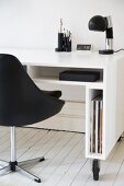 Glossy, white desk with narrow compartments on castors and black, leather swivel chair on white board floor