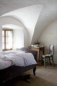 Wood-framed bed with curved foot and seating area in rustic bedroom with vaulted ceiling