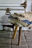 Folded cloths on rustic wooden stool on old tiled floor