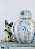 Original vase made from lacquered newspaper and writing paper next to china dog
