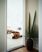 Floor vase with palm leaves next to open door showing view of bed