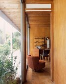 View of brown armchair in 50s-style wood-panelled living room through open door