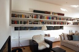 Modernes Wohnzimmer mit langen Bücherregalen und Sideboard; dazwischen ein Fensterschlitz