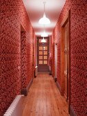 Narrow hall with ornate red and white patterned wallpaper and artificial lighting