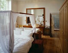 Four-poster bed with white hangings in front of bathtub and washstand in bedroom