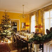 Festive, set dining table and Christmas tree in yellow-painted dining room