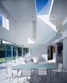 Dining room in front of large windows, staircase with glass balustrade leads to upper storey in background