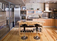 Designer-Küche mit Holz- und Edelstahlfronten, in der Mitte Holztisch mit Weinflaschen und Barhockern