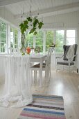 White fabric draped over dining table in loggia of white wooden house