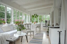 Spacious veranda with comfortable bench and rustic side table next to dining area in white wooden house