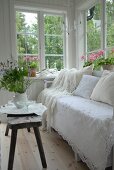 Bench covered with white lace throw and rustic side table in corner of loggia with view of garden