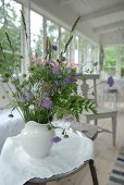 Bouquet of garden flowers in white china jug on side table in loggia