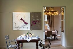 Orchids on small breakfast table and view into lounge with wreath-shaped chandelier