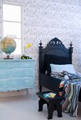 Black bed next to pale blue chest of drawers in child's bedroom