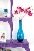 Orchids in blue glass vase on stacked, halved, antique-style tables painted purple