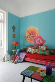 Mediterraner Wohnraum mit Sofa und bunten Kissen vor hellblau getönter Wand mit großen Blumenmotiven