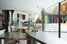 Open-plan, designer kitchen and dining area next to curved glass wall with view of raised living room level