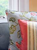 Glänzende Zierkissen, gestreift und mit floralem Muster auf Sofa mit grau gewebtem Stoffbezug