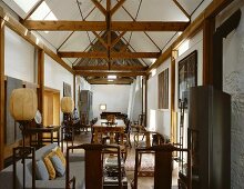 Long, narrow living-dining room with collection of wooden chairs and balloon lamps in historic building with new roof timbers