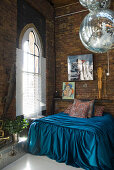 Turquoise silk bedspread on French bed and disco balls in front of church windows in brick loft