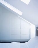 White, fitted, designer wardrobes and bed under sloping ceiling with skylight