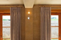 Small, modern wall light between wooden windows with curtains on wooden poles