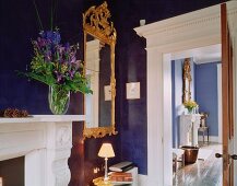 Spiegel im barocken Goldrahmen vor blau getönter Wand in traditioneller Wohnraumecke