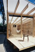 Alter Kaffeehausstuhl auf Holzterrasse und Blick in offenen Wohnraum eines Holzhauses
