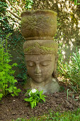 Stone head of Buddha with integrated planter in flowerbed