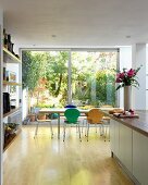 Colourful, Bauhaus shell chairs at dining table in front of floor-to-ceiling glass wall with view of garden