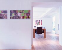 Modern pictures on wall next to wide doorway and view of dining table