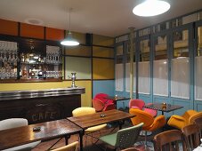 Shell chairs with colourful upholstery and multi-coloured wall panels in retro-style bar