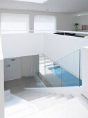 Staircase leading down from open-plan living room with view of sunny indoor swimming pool