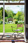 Delicate metal and linen chair on terrace with view of sunny garden