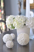 weiße Dekokugeln mit unterschiedlichen Oberflächen vor weißem Blumenstrauss auf Tisch