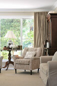 Antique upholstered armchair next to side table with table lamp in front of terrace window