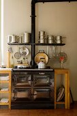 Vintage cooker in simple kitchen unit with integrated wall-mounted shelf and stacked stainless steel saucepans