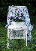 Floral blouse and blue and purple violas on old wooden chair amongst grass
