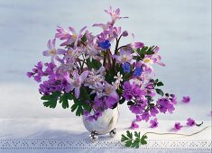 Purple spring bouquet in vase on lace tablecloth